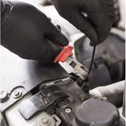 Ruky v čiernych rukaviciach používajú kliešte na pripevnenie drôtu k automobilovému motoru. Kliešte sú červeno-čierne. Motor je čiastočne odkrytý.