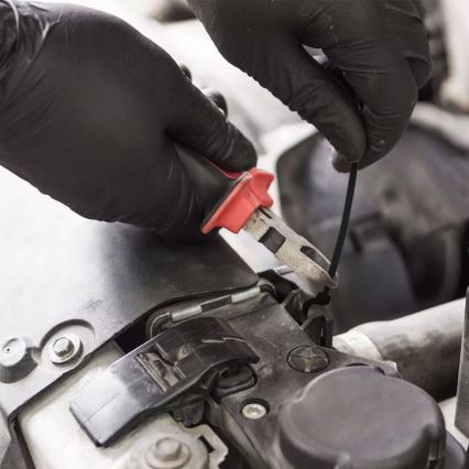 Ruky v čiernych rukaviciach pripevňujú plastovú sponu k motorovému priestoru auta pomocou klieští.