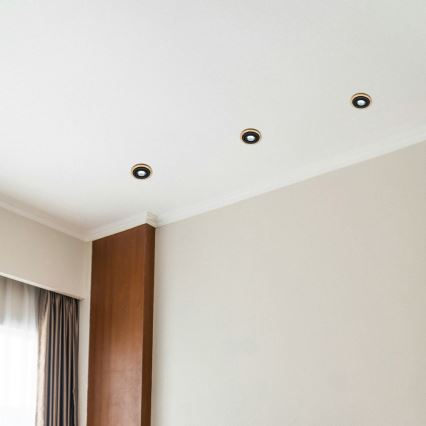 Štyri zapustené bodové svetlá sú osadené na bielom strope. Svetlá sú umiestnené v rohu miestnosti s hnedým dreveným prvkom na stene a svetlo béžovou stenou.