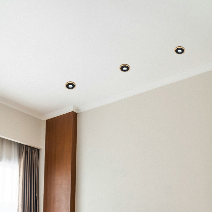 Štyri zapustené bodové svetlá sú osadené na bielom strope. Svetlá sú umiestnené v rohu miestnosti s hnedým dreveným prvkom na stene a svetlo béžovou stenou.