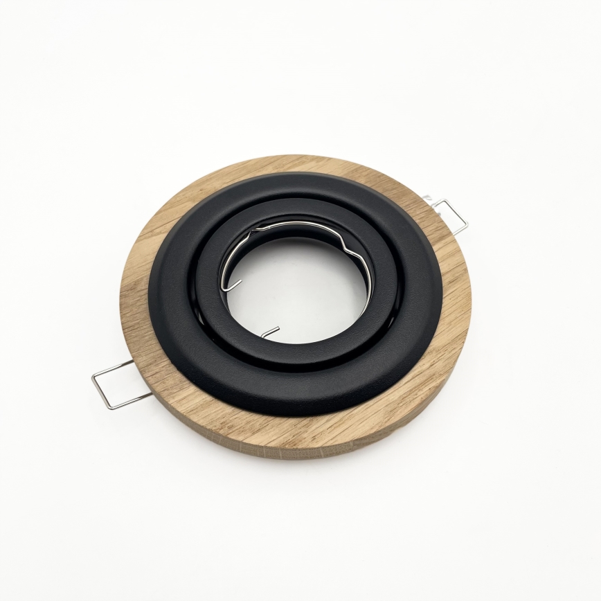 Svietidlový rámček z dubového dreva s čiernym kovovými prstencami leží na bielom pozadí. Rámček má dva kovové držiaky.