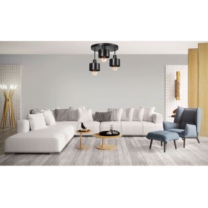 Trojramenné stropné svietidlo s čiernymi tienidlami visí v modernej obývacej izbe nad bielou sedačkou a dvoma konferenčnými stolíkmi. V izbe sa nachádza aj kreslo s taburetom.