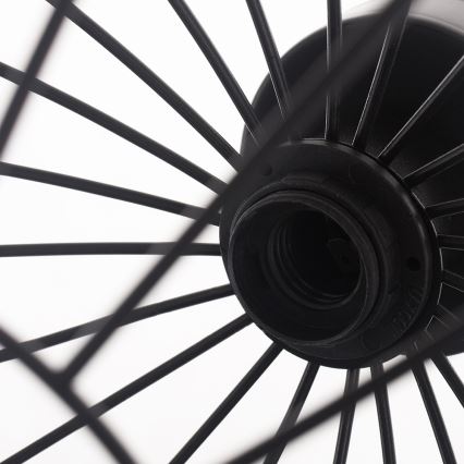 Čierna kovová lampa s drôteným tienidlom v tvare kolieska. Tienidlo je pripevnené k čiernej objímke pre žiarovku. Biele pozadie.