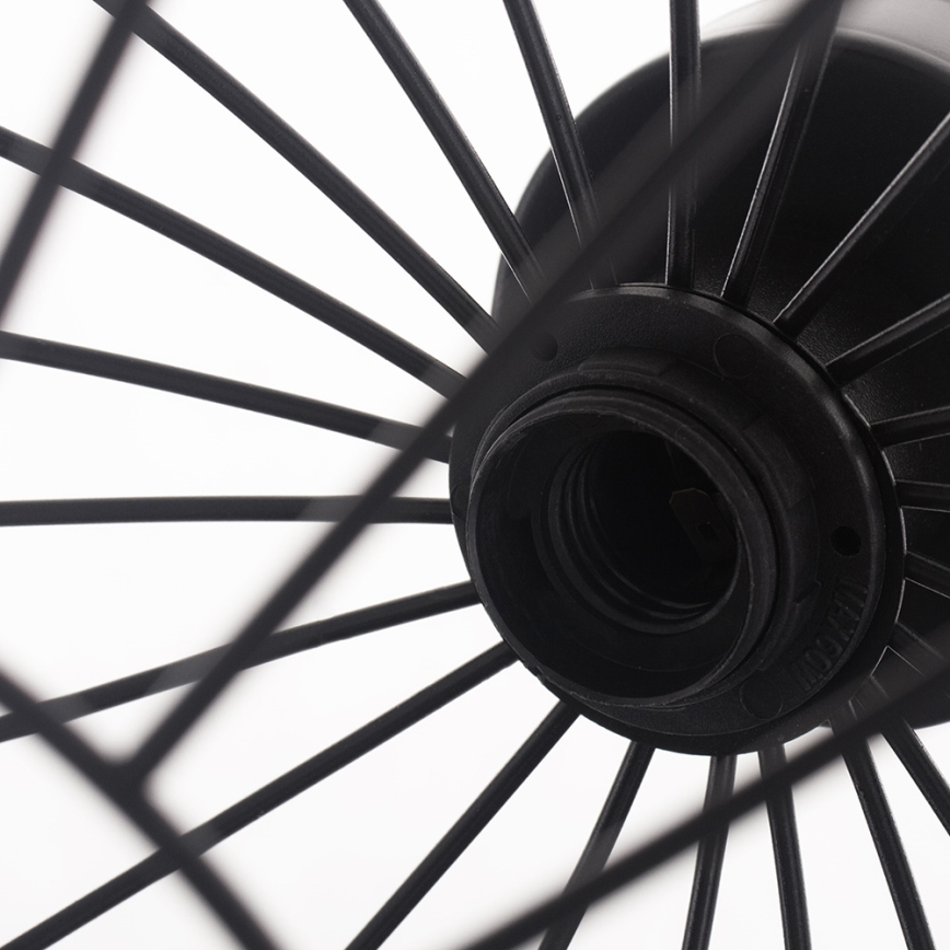 Čierna kovová lampa s drôteným tienidlom v tvare kolieska. Tienidlo je pripevnené k čiernej objímke pre žiarovku. Biele pozadie.