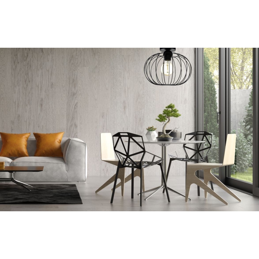 Svietidlo visí nad jedálenským stolom so štyrmi stoličkami v modernom interiéri. Dve stoličky sú čierne, dve svetlé drevené. Na stole je bonsaj.