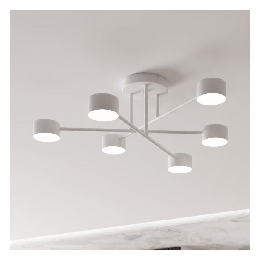 Biela stropná lampa s piatimi valcovými tienidlami je pripevnená k stropu. Ramenné konštrukcie držia tienidlá, ktoré svietia. Lampa je umiestnená v interiéri na svetlom strope.