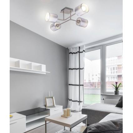 Stropné svietidlo s piatimi cylindrickými tienidlami svieti v obývacej izbe. Svietidlo je pripevnené k stropu a je súčasťou modernej izby s nábytkom v neutrálnych farbách.