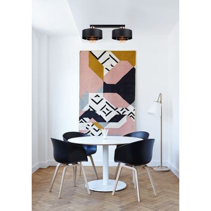 Dvojité stropné svietidlo svieti v jedálni. Svietidlo je čierne s medenými detailmi. V miestnosti sa nachádza jedálenský stôl s čiernymi stoličkami a abstraktný obraz na stene.