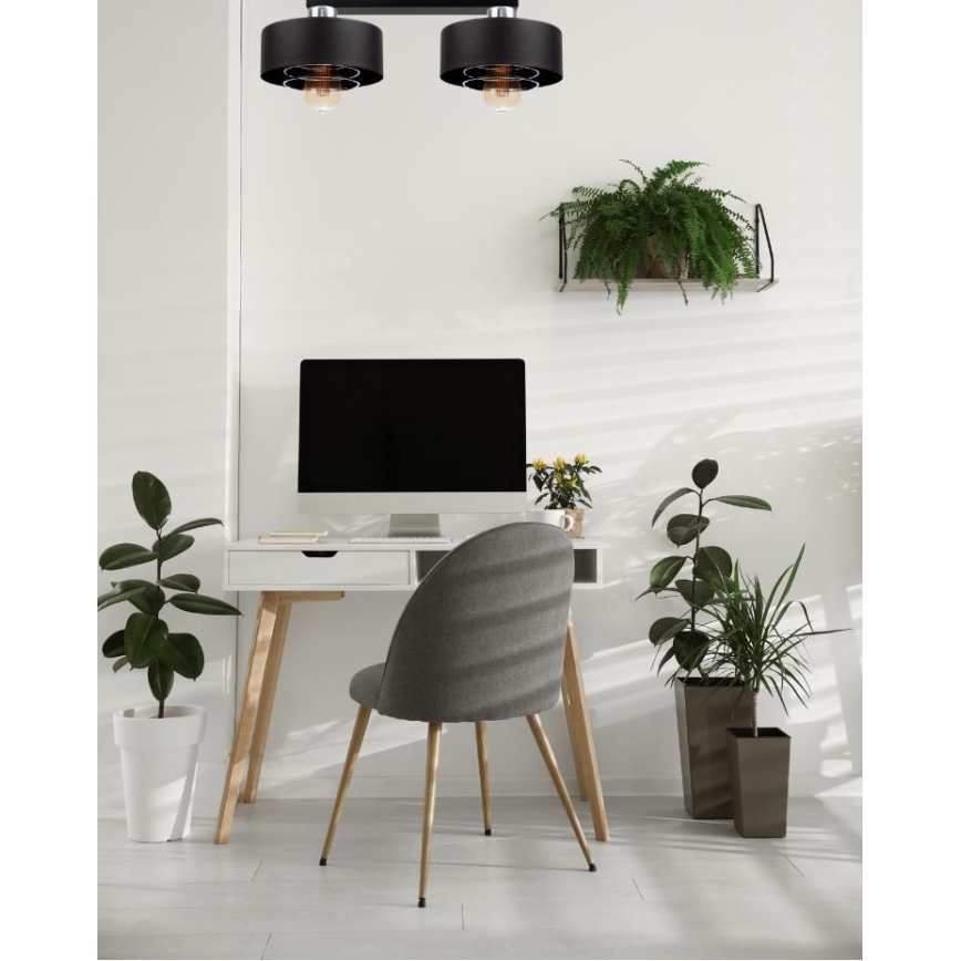 Dvojité stropné svietidlo s čiernymi tienidlami a viditeľnými žiarovkami osvetľuje pracovnú plochu s počítačom, stoličkou a kvetináčmi. Svietidlo je upevnené na strope.