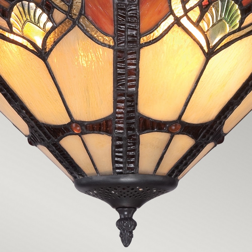 Tiffany lampa svieti. Jej tienidlo je kužeľovité, zo skla s hnedými a krémovými panelmi a ornamentmi. Spodná časť je z čierneho kovu.