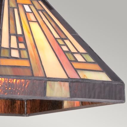Kužeľovitý tienidlo lampy, zložené z farebného vitráža s geometrickým vzorom v hnedo-oranžových tónoch, je zobrazené detailne. Tienidlo je osvetlené zvnútra, čím sa zvýrazňuje jeho textúra a farby. Je umiestnené na svetlom pozadí.