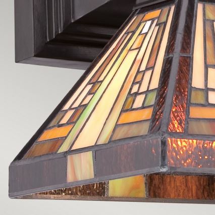 Svietidlo s tienidlom z farebného skla v štýle art deco je pripevnené k tmavohnedému stropnému púdru. Tienidlo je pyramídového tvaru, zdobené geometrickými vzormi v hnedých, oranžových a zelenkavých odtieňoch.