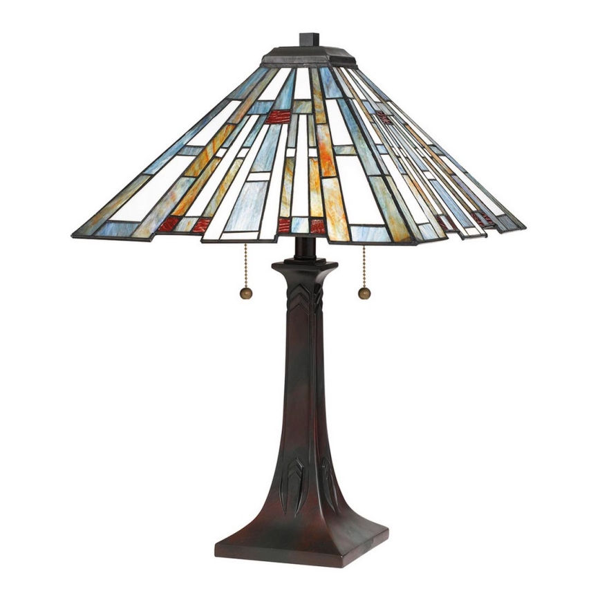 Stolová lampa s kužeľovitým tienidlom z farebného vitráža s geometrickým vzorom v modrých, bielych, žltých a červených odtieňoch. Má hnedý kovový podstavec a dva retiazkové vypínače. Lampa stojí na bielom pozadí.