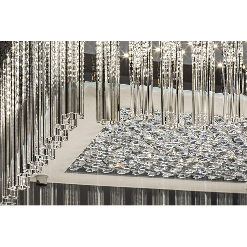 Kríšťalový luster s mnohými visiacimi sklenenými tyčinkami a kryštálovou základňou je osvetlený. Svetlo prechádza cez kryštály.