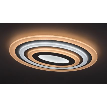 Oválny stropný svietidlo svieti na tmavom strope. Svietidlo má tri koncentrické oválne vrstvy v odtieňoch bielej a svetlohnedej. Vnútorná vrstva je najtmavšia.