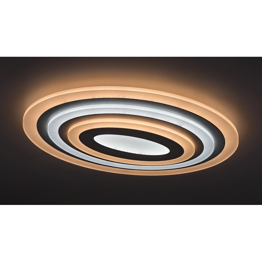 Oválny stropný svietidlo svieti na tmavom strope. Svietidlo má tri koncentrické oválne vrstvy v odtieňoch bielej a svetlohnedej. Vnútorná vrstva je najtmavšia.