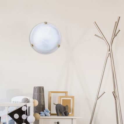 Svietidlo svieti v detskej izbe. Okrúhle, mliečne biele svietidlo je pripevnené na stene. V miestnosti sa nachádza detská postieľka, stojan na oblečenie a nábytok s hračkami.