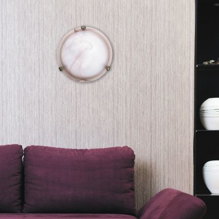 Okrúhle nástenné svietidlo je pripevnené na stene. Svietidlo je z mliečneho skla s jemnými ružovými odtieňmi. Nachádza sa v interiéri, vedľa tmavočervenej pohovky a čiernej poličky s dekoratívnymi nádobami.