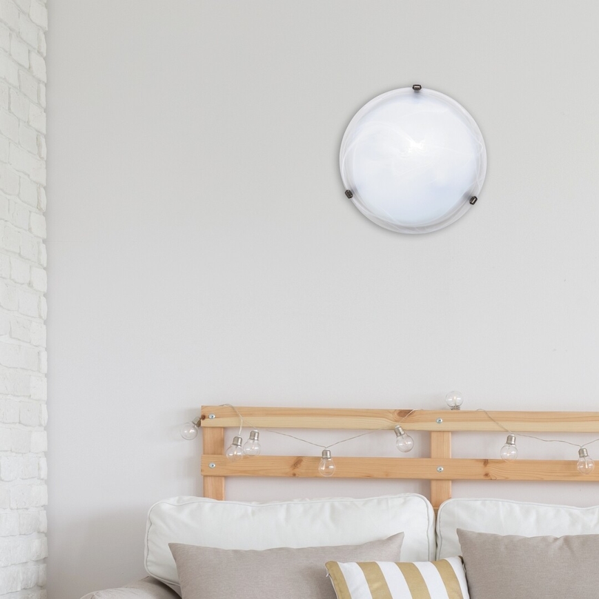 Okrúhle stropné svietidlo je pripevnené na stene nad posteľou s dreveným čelom a ozdobnými svetelnými bodkami. Svietidlo je biele a má kovový rám.