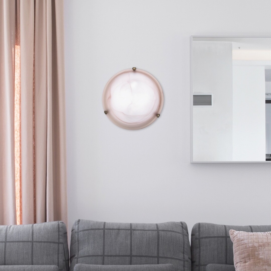 Okrúhla nástenná lampa svieti na stene obývacej izby. Lampa je umiestnená medzi šedou pohovkou a zrkadlom. Blízko je béžová záclona.