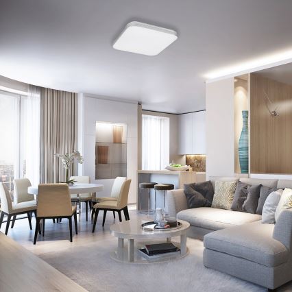 Štvorcové stropné svietidlo osvetľuje moderný obývací priestor. Svietidlo je umiestnené v strede miestnosti, ktorá obsahuje jedálenský stôl so stoličkami a rohovú sedačku.