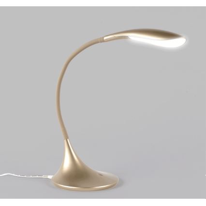 Stolná lampa zlato-béžovej farby s ohnutým ramenom svieti. Je umiestnená na neutrálnom svetlosivom podklade.