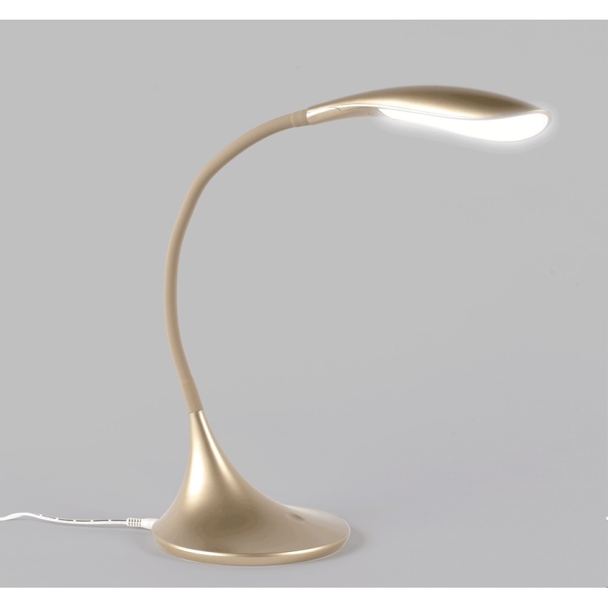 Stolná lampa zlato-béžovej farby s ohnutým ramenom svieti. Je umiestnená na neutrálnom svetlosivom podklade.