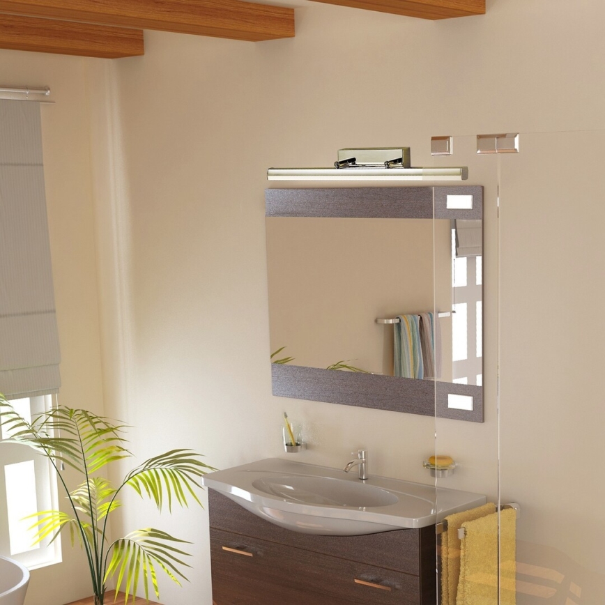 Svietidlo osvetľuje zrkadlo v kúpeľni. Umývadlo s nábytkom je umiestnené pod zrkadlom. Rastlina stojí vedľa umývadla.