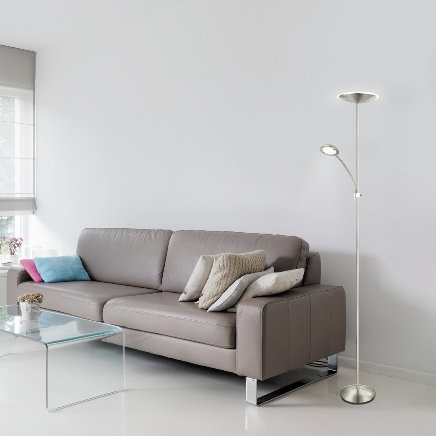 Stojacia lampa s dvoma svetlami stojí v obývacej izbe pri koženej sedačke a sklenenom konferenčnom stolíku.