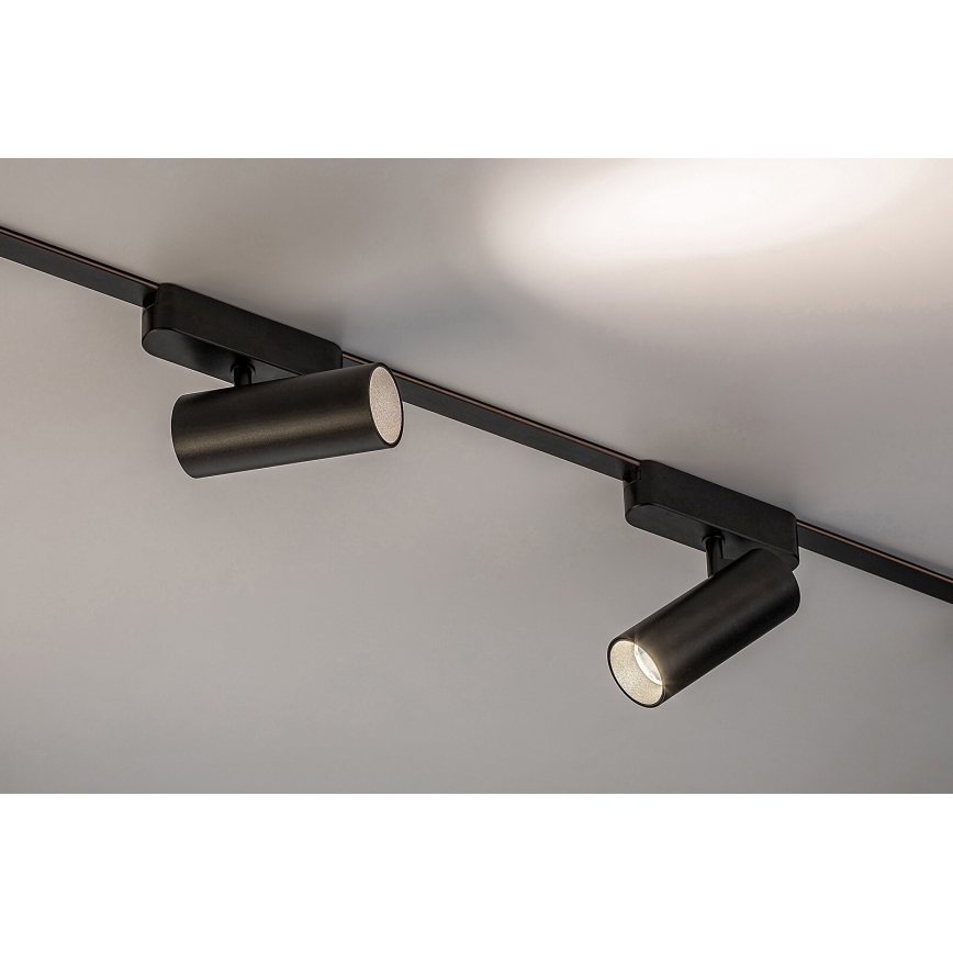 Dve čierne bodové svietidlá pripevnené na stropnej lište smerujú svetlo do miestnosti. Svietidlá sú valcovitého tvaru. Lišta je upevnená na svetlom strope.