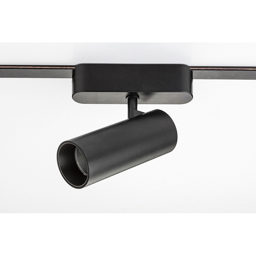 Čierne svietidlo je pripevnené k stropnej lište. Svietidlo je valcovitého tvaru a smeruje doprava. Lišta je tmavohnedá.