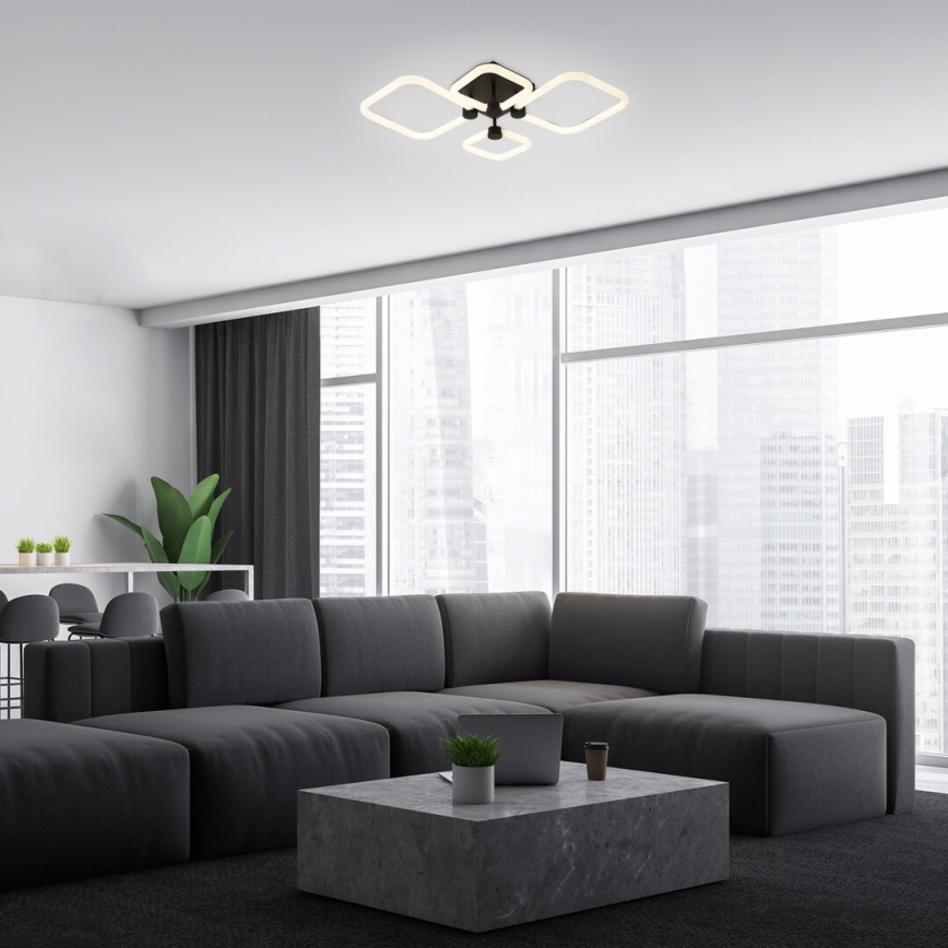 Svietidlo svieti v modernom interiéri. Štvorramenné stropné svietidlo s hranatými tienidlami je umiestnené nad rozsiahlou tmavosivou sedačkou a nízkym kamenným stolíkom v miestnosti s veľkými oknami s výhľadom na mesto.