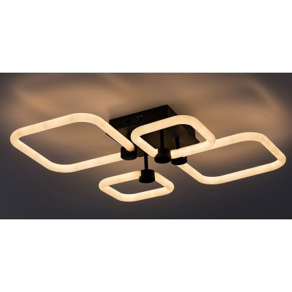 Svietidlo svieti. Štyri štvorcové LED svetlá sú pripojené k štvorcovému čiernemu stropnému držiaku. Svetlá svietia teplým bielym svetlom na tmavom pozadí.