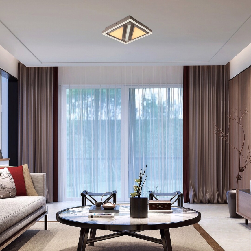 Svietidlo štvorcového tvaru s dvoma zdrojmi svetla je osadené na strope. Nachádza sa v obývacej izbe s nábytkom a závesmi.