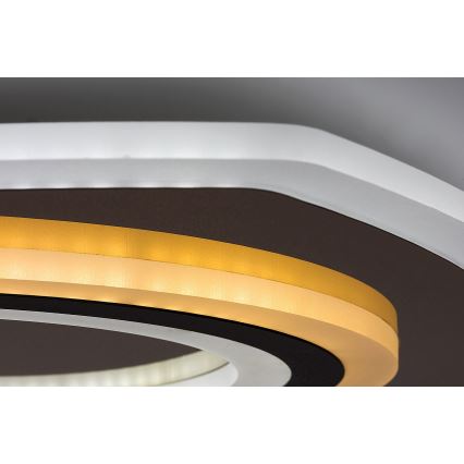 Svietidlo svieti. Je inštalované na strope. Má okrúhly tvar s viacerými farebnými kruhmi: bielym, tmavohnedým a zlatým.