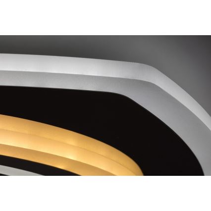 Svietidlo svieti. Má strieborný rám a čierny stred s dvoma žltými LED pásikmi. Je umiestnené na strope.