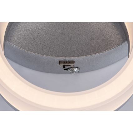 Svietidlo je pripevnené skrutkou k stropu. Svietidlo má sivý kovový kryt a vnútorný svetelný kruh. Je vidieť detail mechanizmu pripevnenia.