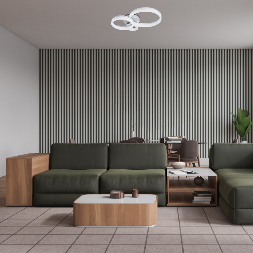 Rohová sedačka tmavozelenej farby stojí v obývacej izbe s drevenou podlahovou krytinou a stenou s vertikálnymi čierno-bielymi pruhmi. Pred sedačkou je nízky drevený stolík. V pozadí je jedálenský stôl so stoličkami. Na strope je trojitá kruhová lampa.