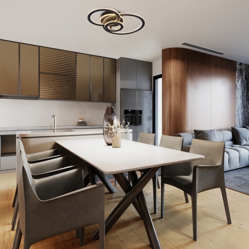 Svetlo svieti nad jedálenským stolom. Stôl s tmavými stoličkami stojí v modernom interiéri s kuchyňou a obývacou izbou.