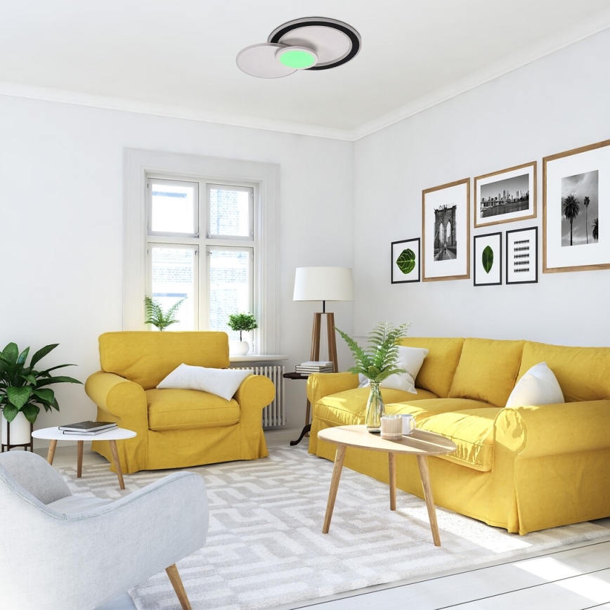 Stropné svietidlo svieti v obývacej izbe. Žltá sedačka a kreslo sú umiestnené na koberci. V pozadí sú obrázky na stene.