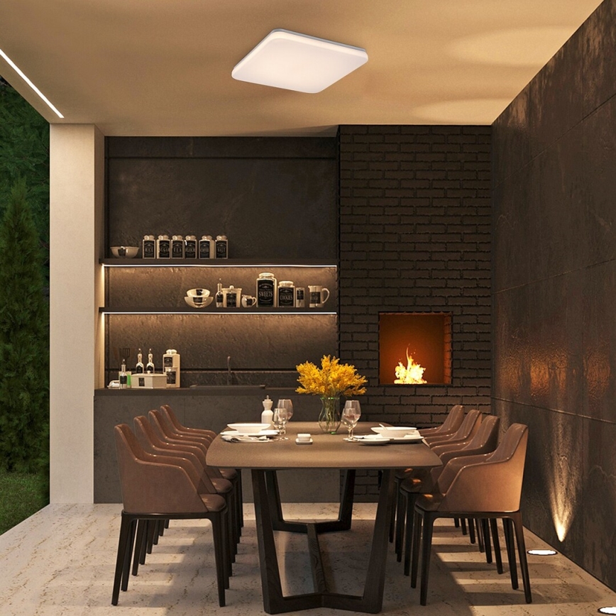 Štvorcový stropný svietidlo svieti nad jedálenským stolom v moderne zariadenej jedálni s krbom a vstavanými policami. Stôl je obklopený hnedými stoličkami.