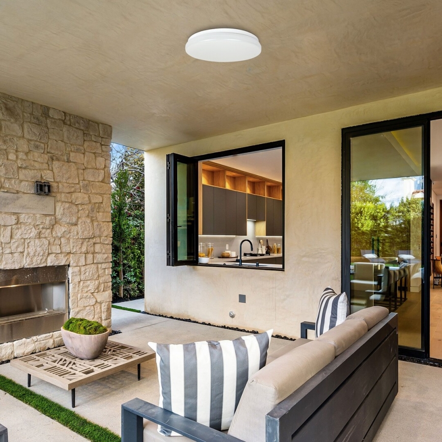 Svietidlo svieti na terase. Terasa má kamenný krb, sedaciu súpravu a výhľad na kuchyňu cez otvorené okno.