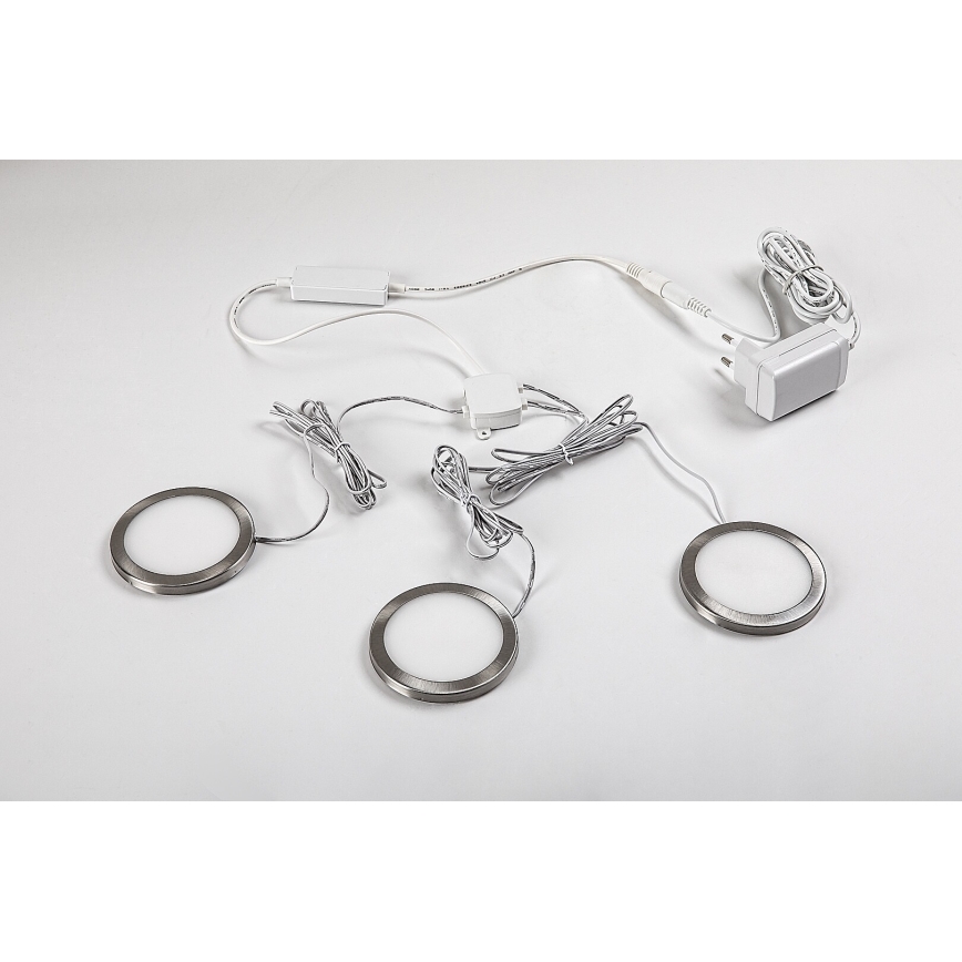 Tri okrúhle LED svetlá s kovovými rámami sú umiestnené na svetlom povrchu. Sú prepojené káblami a napájacím zdrojom s európskou zástrčkou.