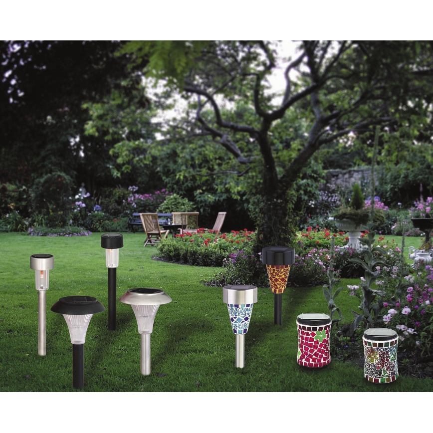 Solárne záhradné svietidlá rôznych tvarov a dizajnov sú umiestnené na trávniku. Svietidlá sú zapustené do zeme, v pozadí je vidieť záhradu s stromami a kvetmi.