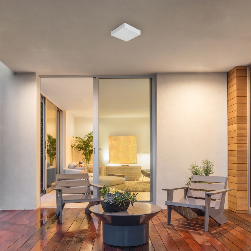 Svietidlo osvetľuje vonkajšiu terasu. Dve drevené stoličky sú umiestnené okolo nízkeho stolíka s kvetináčom. V pozadí sa nachádza presklená stena s výhľadom na interiér domu.