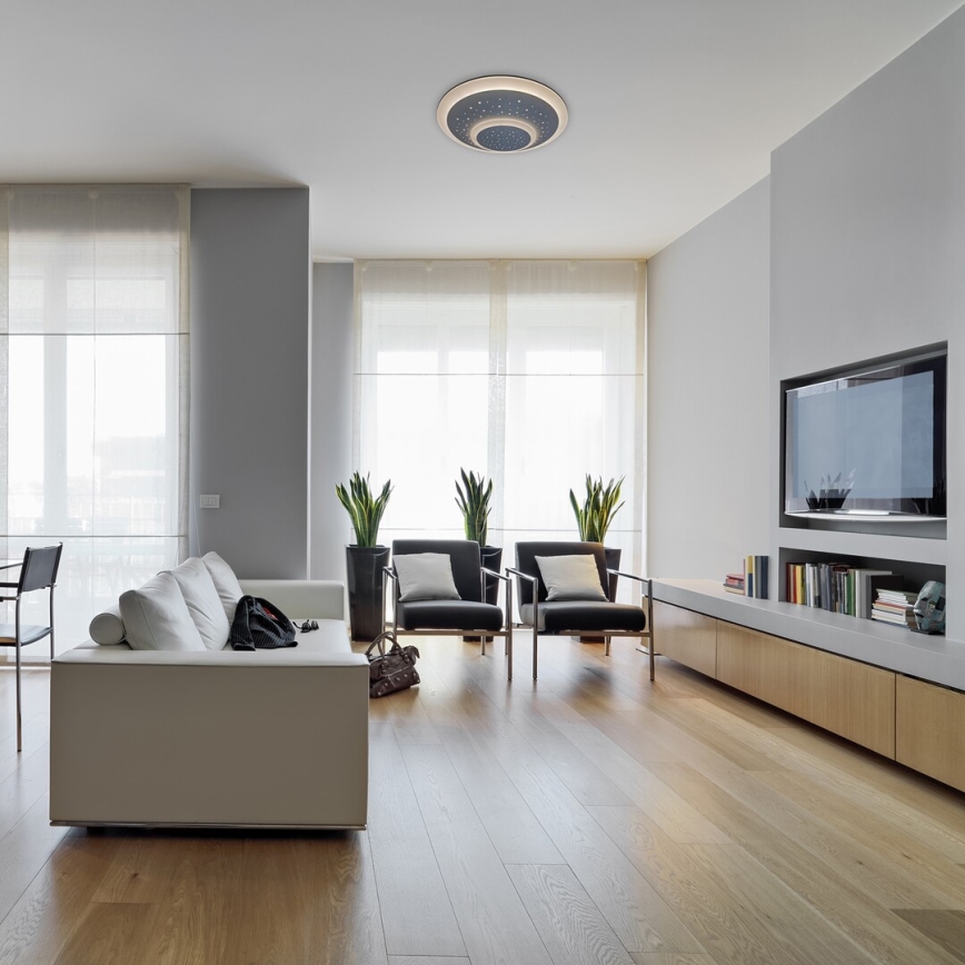 Svetlo svieti v obývacej izbe. Biela sedačka je umiestnená v priestore s drevenou podlahou, krbom a televízorom. Okná za sedačkou umožňujú výhľad von.