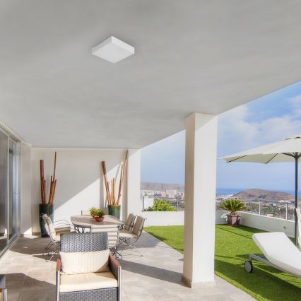 Stropné svietidlo svieti na terasu. Na terase sa nachádza jedálenský stôl s kreslami, v pozadí je trávnik a výhľad na more.