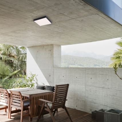 Stropné svietidlo svieti na terase. Drevený jedálenský stôl s kreslami stojí na drevenej terase s výhľadom na kopcovitú krajinu.