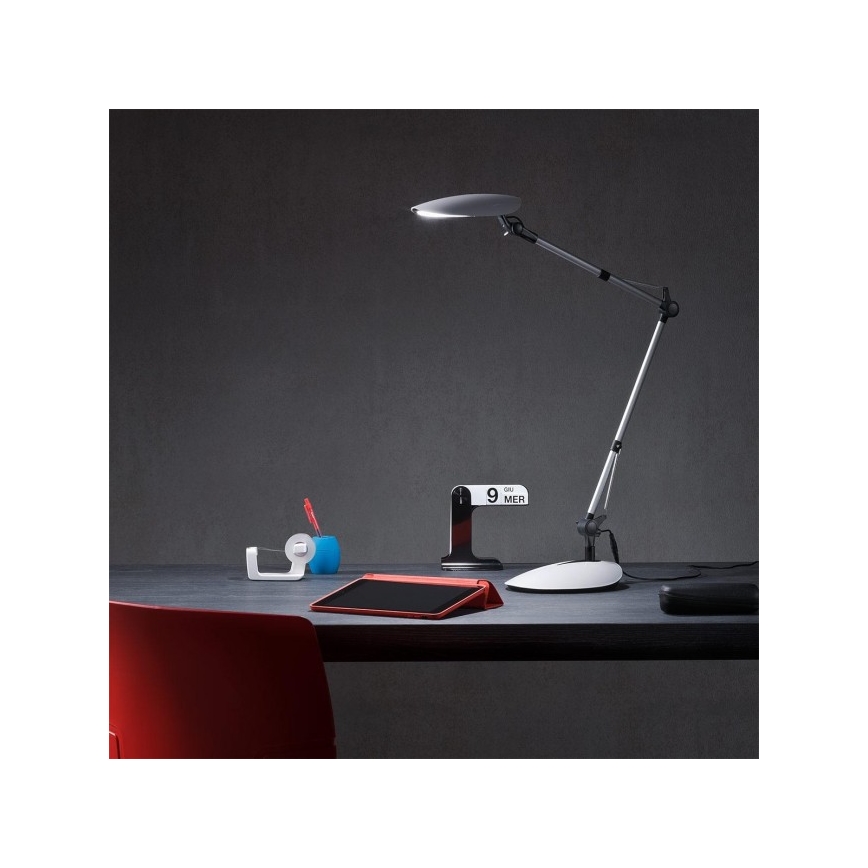 Stolová lampa svieti na pracovný stôl. Na stole je tablet, lepiaca páska, držiak na pero a stolný kalendár s nápisom „9 MER“.