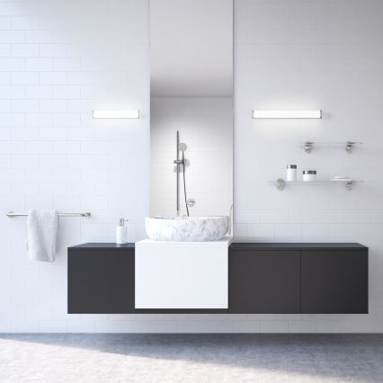 Mramorové umývadlo je umiestnené na tmavošedej skrinke v kúpeľni. Kúpeľňa má biele obklady a dve sklenené police s kozmetikou.